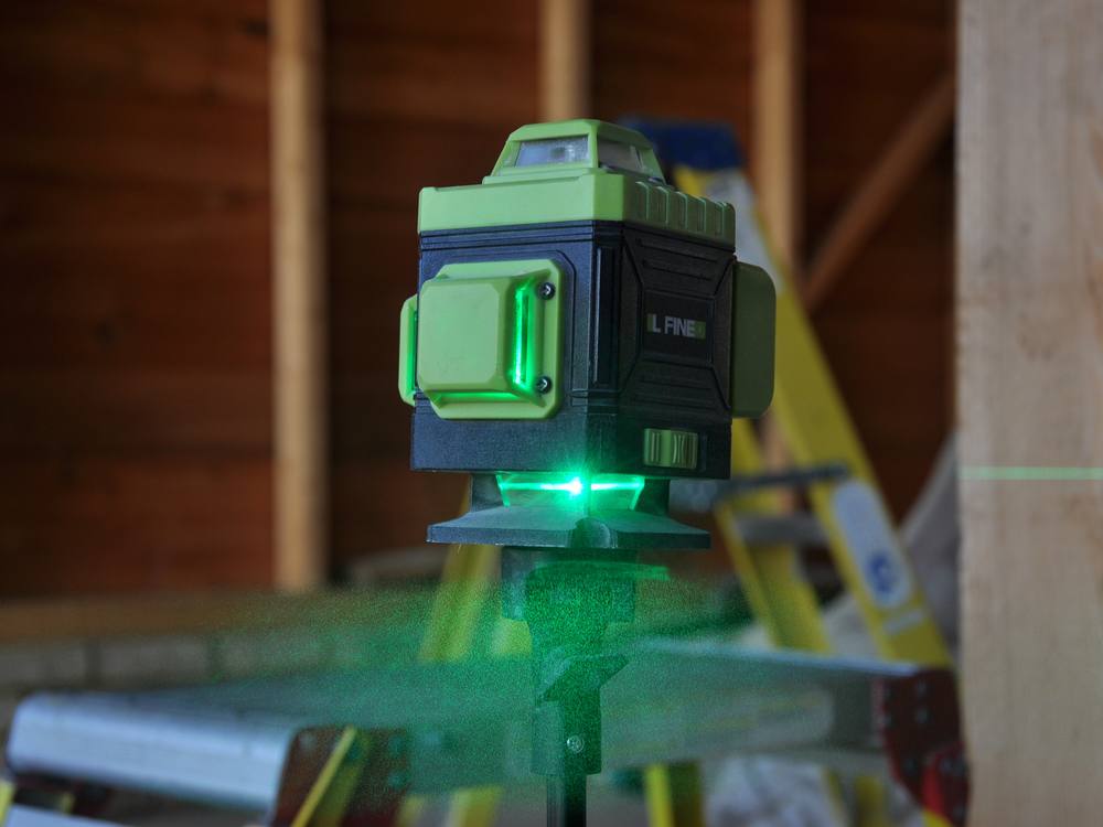 A green cross-line laser level setting out downlights in a loft
